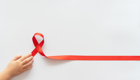 AID red ribbon in child hands on white background, symbol of struggle against HIV, AIDS and cancer. Concept of helping those in need. Charity, donation, donor. Mock up, blank, template 4Kの写真素材