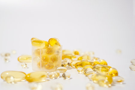 Close-up transparent golden pills into measuring cup over white background. Omega 3 pills or Vitamin D gelatin capsuleの写真素材