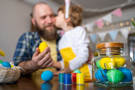 Easter Family traditions. Father and caucasian happy child with bunny ears dye and decorate eggs with paints for holidays while sitting together at home table having fun. Copy spaceの写真素材