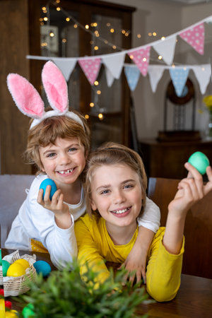 Easter Family traditions. Two caucasian happy children with bunny ears dye and decorate eggs with...