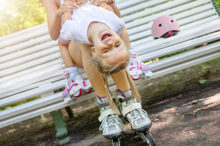 Mother and daughter playing on bench after skating inline roller in public park together. Family leisure sport activity weekend. Copy negative spaceの写真素材