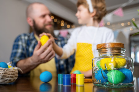 Easter Family traditions. Father and caucasian happy child with bunny ears dye and decorate eggs with paints for holidays while sitting together at home table having fun. Negative spaceの写真素材