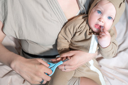 Close up Mother cutting small baby nails with children scissors. Evening in the bedroom routine. Concept of body care and parenthood.の写真素材