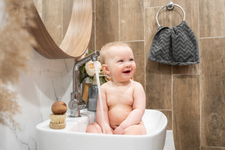 Baby bathing in bathroom sink. Child playing with water in cozy bathroom. Little toddler take shower. Water fun for kids. Hygiene and skin care for children. Bath room interiorの写真素材