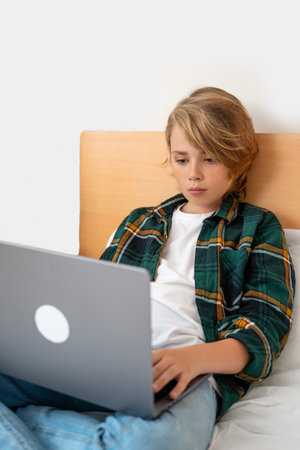 Smart caucasian middle School child boy using laptop. Child typing on the keyboard. Play video game.Online tutor teaching digital class, web lesson on computer at home. Virtual education. E-education. Verticalの写真素材
