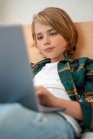 Smart caucasian middle School child boy using laptop. Child typing on the keyboard. Play video game.Online tutor teaching digital class, web lesson on computer at home. Virtual education. E-education. Verticalの写真素材