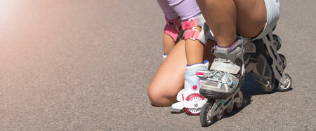 Close up Mother hugging child daughter to skate on inline skates rollers in public park in summer. Family leisure outdoor sport activity game. Copy negative spaceの写真素材