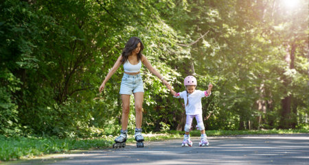 Mother teaching child daughter to skate on inline skates rollers in public park in summer. Family leisure outdoor sport activity game. Copy negative spaceの写真素材