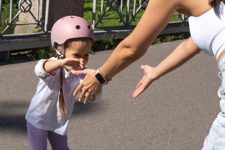 Mother teaching child daughter to skate on inline skates rollers in public park in summer. Family leisure outdoor sport activity game. Copy negative spaceの写真素材