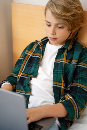 Smart caucasian middle School child boy using laptop. Child typing on the keyboard. Play video game.Online tutor teaching digital class, web lesson on computer at home. Virtual education. E-education. Verticalの写真素材