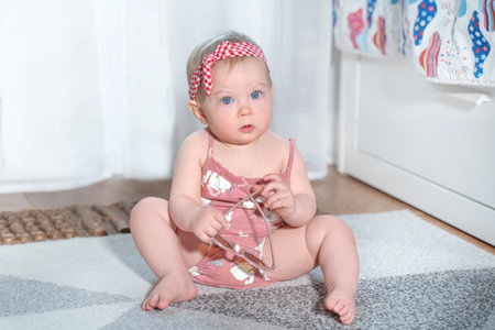 Little caucasian girl sitting on floor in children room. Cute toddler wear swimsuit suit and hold sunglasses. Summer Vacation preparation. Goods and products for children. Early developmentの写真素材