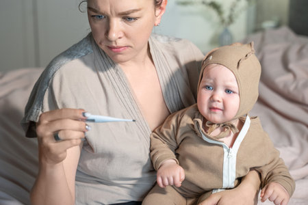 Mom measures body temperature baby by electronic thermometer. Sick child with high temperature. Children illness, clod and flue, runny nose, cough, disease, parent careの写真素材