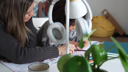 Caucasian mother and African American daughter studying at home, doing homework in cosy white room. Parent teach, child school girl learn knowledge, write exercise read book. Education for children. Private lessonの写真素材