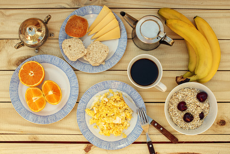 Tasty breakfast on the wooden table with scrambled eggs, cheese, bread, coffee, oat with cherry,...