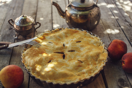 Homemade peach pie or tart with fresh fruits with vintage kettle, fork and knife on the wooden background. Eating concept. の写真素材
