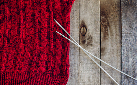 Beautiful red knitted sweater with needles  on wooden background. Knitting texture. Knitting pattern. Copy space. Half. の写真素材
