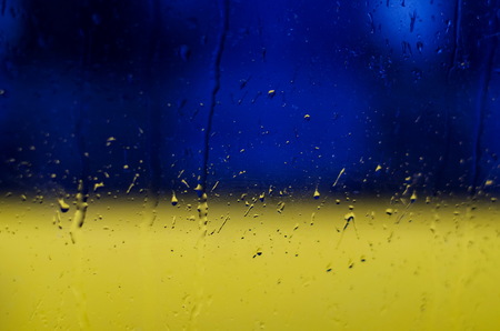 Raindrops on window glass, on blue and yellow background in colors of the Ukrainian national flagの写真素材