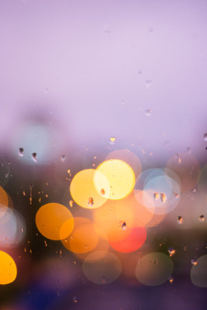 Raindrops in blue glass background. City street lights bokeh defocused, abstract dusk night city backgroundの写真素材