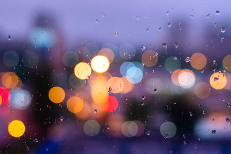 Raindrops in blue glass background. City street lights bokeh defocused, abstract dusk night city backgroundの写真素材