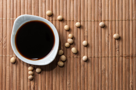A bowl of soy sauce and soy grains on a bamboo placematの写真素材
