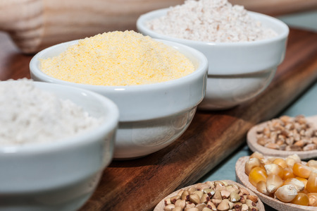 Three white bowls with corn flour and buckwheat and utensilsの写真素材
