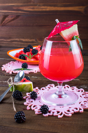 Watermelon fresh in a glass with an umbrella, a spoon, a salad of watermelon, blackberry and mint. On a wooden background.の写真素材
