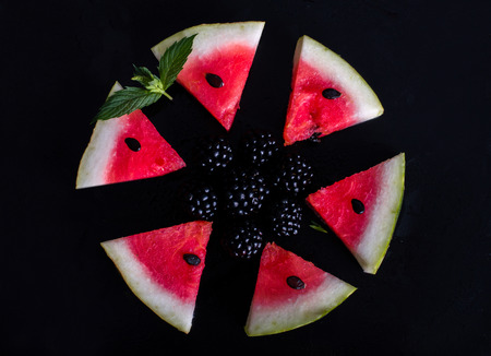 Triangular pieces of watermelon with seeds. Blackberry and mint. black fone.Top view. Flat lay.の写真素材