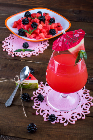 Watermelon fresh in a glass with an umbrella, a spoon, a salad of watermelon, blackberry and mint. On a wooden background.の写真素材