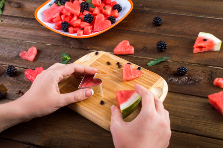 Plate with salad of watermelon, blackberries, mint. hand cut hearts of watermelon on a wooden board. On a wooden background.の写真素材