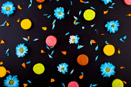 Yellow, green, pink, orange macaroon. Blue flowers and blue and orange petals. On a black background. Top view. Flat lay.の写真素材