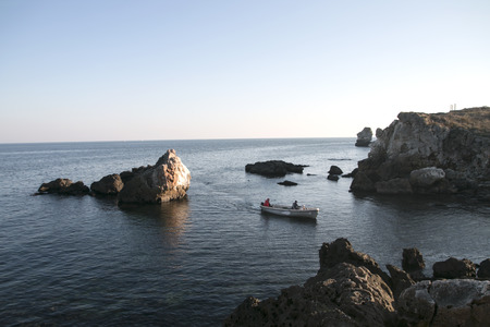 Fishermen going back home with the boat in sunset,crossing sea with big cliffsの写真素材