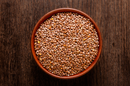 Rustic ceramic bowl of uncooked red lentils isolated on dark wood from aboveの写真素材