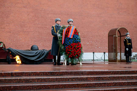 MOSCOW, RUSSIA - DECEMBER 04, 2019: The Honor Guard of the 154 Preobrazhensky Regiment in the infantry uniform laying flowers to the Tomb of Unknown soldier and Eternal flame in Alexander garden near Kremlin wall in rainy weatherのeditorial素材