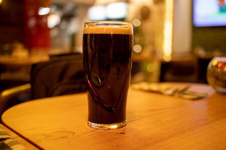 pint glass of dark stout beer with foam stands on a wooden table in a barの写真素材