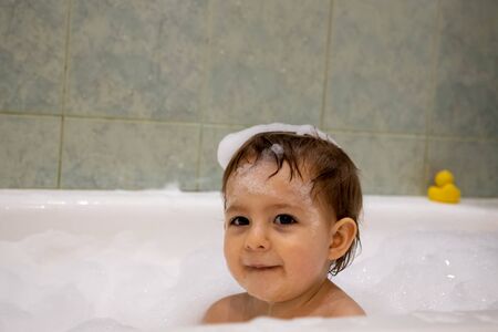 Cute little baby girl smiles looking at camera taking a bath with a soap foam arround and her head....