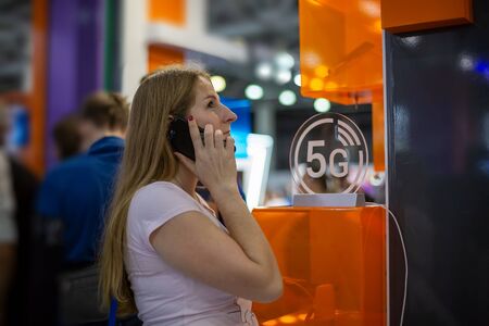 young caucasian girl talking on a smartphone on the background of the 5g icon. background blur, soft focusの写真素材