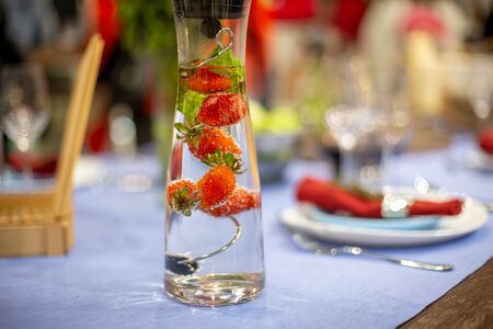 a carafe filled with water and strawberries stands on a served blue table.  close up, soft focus....