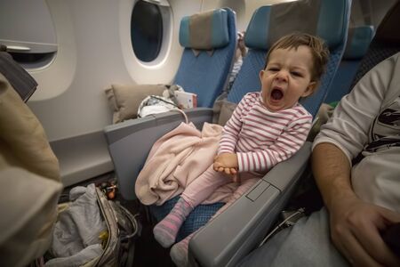 little cute sleepy toddler sitting in an airplane seat and yawning tiredlyの写真素材