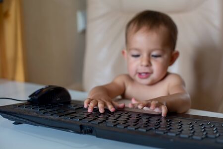 close up of baby fingers on keyboard.on backround cute little baby sitting on an office chair and clicks on the keyboard in blur, close up, soft focus.の写真素材