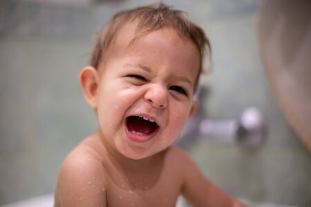 portrait of a cute Caucasian child with a sly smile, opening his mouth and looking at the camera. the baby is wet, bathes, in the background the bathroom is blurred. close-up, soft focusの写真素材
