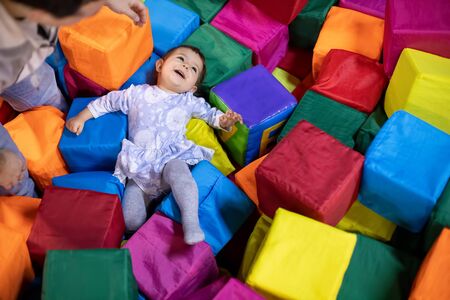 little cute toddler girl in a dress lies with smile and happy laugh in the pool with cubes her fater stays near.. playground in the childrens play center. top viewの写真素材