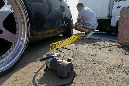 accident on the road: flat tire pressure. a man inflates a passenger car wheel with a compressor with a long yellow hose. close-upの写真素材