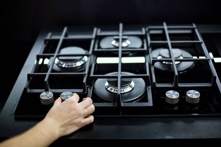 female hand turn the handle of the new modern gas stove with four burners for the kitchen, stainless...