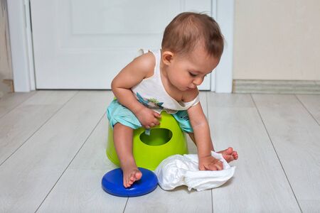 potty training concept. A cute little baby sits on a green pot and plays with a diaper in the room. close-up, soft focus, place for copy spaceの写真素材