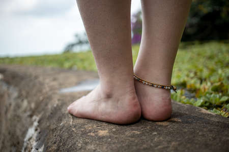 female legs with a bracelet on the side of the pond against the backdrop of a natural landscapeの写真素材