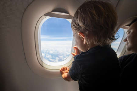 cute toddler points his finger at the sky through the window. first flight concept, traveling with children.の写真素材