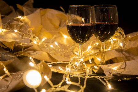two wine glasses stand in a shining yellow garland on craft paper. cozy romantic celebrationの写真素材