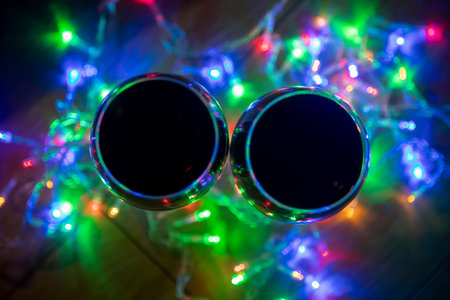 Two glass wine glasses in shining christmas garland on dark
