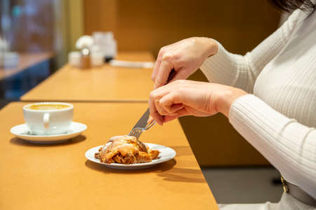 woman cuts croissant and drinks coffee at a table in a cafe. no face
