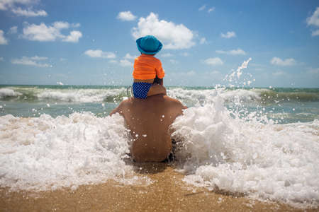 dad with a baby on his shoulders playing in the spray of sea foam. happy childhood concept.の写真素材